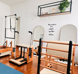 Mulher sorridente em posição de alongamento em cadillac de Pilates com instrutor observando